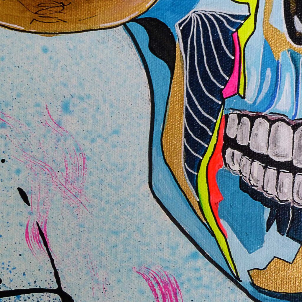 Détail du profil du crâne doré et bleu aux dents blanches, sous le plateau de la balance